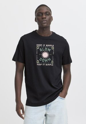 Schwarzes Baumwoll-T-Shirt mit einem Grafikdesign, auf dem in Türkis und Pink der Text „SLOW DOWN“ steht, umgeben von geometrischen Akzenten.