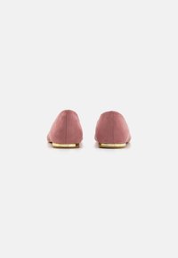 Pantofi fără toc din suede roz, cu vârful rotunjit și o talpă plată cu accente aurii, evidențiind o textură netedă și un design minimalist.