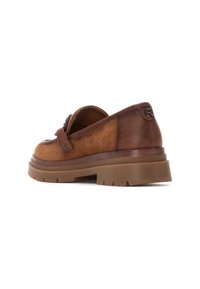 Zapatos tipo slip-on de ante marrón con una correa de cuero en contraste, suela de goma gruesa y detalle del logotipo en el talón. Acabado texturizado.