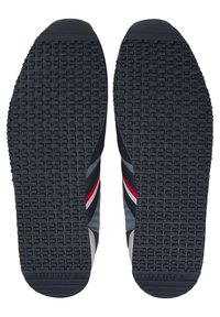 Semelles de chaussures présentant un design en caoutchouc texturé, principalement noir avec des bandes grises et rouges sur les côtés, et le logo de la marque au talon.