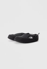 Chaussures noires isolées à enfiler avec un design rembourré, semelle en caoutchouc texturée et détail de logo sur le côté. Comprend une languette à l'arrière pour un enfilage facile.