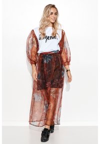Biała koszulka z napisem "gorgeous." w towarzystwie zwiewnej, półprzezroczystej spódnicy maxi w kolorze rdzy z kwiatowym wzorem. Czarne sneakersy z ozdobami.