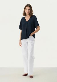 Blusa blu navy a maniche corte con scollatura a V, abbinata a pantaloni bianchi dritti. Le flat marroni completano l'outfit. Tessuto liscio.