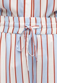 Ύφασμα με κάθετες ριγέ μπλε, λευκές και κόκκινες ρίγες, με ελαστική μέση και κορδόνι δεμένο στο κέντρο.