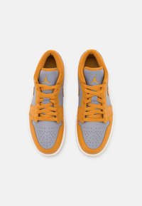 Paire de baskets basses gris et orange avec embout perforé et lacets, vue de dessus sur fond blanc.