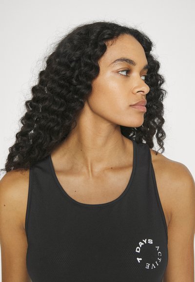 Black athletic tank top with a round white logo featuring "7 DAYS ACTIVE." The fabric appears textured with a fitted design and wide straps.