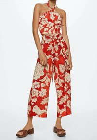 Rode bloemen crop top gecombineerd met wijde, hoog getailleerde broek. De stof heeft grote witte bloemenpatronen. Accessoires zijn onder andere bruine platform sandalen.