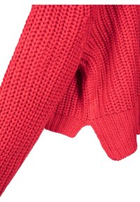 Détail d’un pull rouge en tricot montrant des mailles épaisses texturées et un ourlet côtelé avec un bord légèrement festonné.