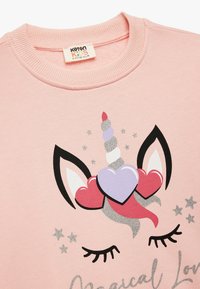 Sudadera de color rosa claro con un gráfico de unicornio que presenta acentos de purpurina plateada, corazones y ojos cerrados. Cuello redondo acanalado.