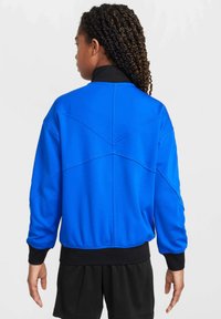 Giacca a zip blu con colletto nero, caratterizzata da un design testurizzato e polsini a coste. Il tessuto appare liscio con una vestibilità rilassata.