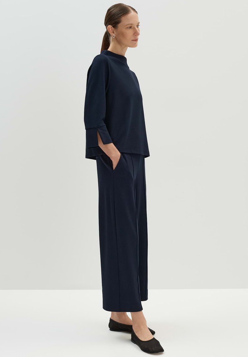 Haut bleu marine à coupe décontractée avec des manches trois-quarts et des fentes sur les côtés, associé à un pantalon large assorti. Porté avec des chaussures plates noires.