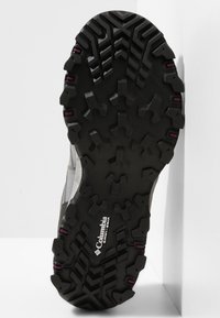 Semelle de chaussure Columbia noire et robuste avec des motifs de bande de roulement profonds et de petites touches violettes sur les crampons.