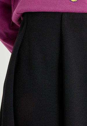 Jupe plissée noire à texture lisse, associée à un sweat-shirt ample rose foncé avec un petit détail graphique.