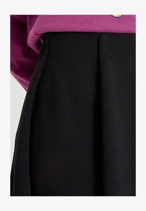 Jupe plissée noire à texture lisse, associée à un sweat-shirt ample rose foncé avec un petit détail graphique.