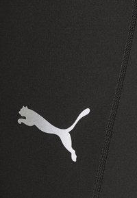 Černé sportovní legíny vyrobené z elastické tkaniny s vroubkovanou strukturou. Na levé straně se nachází výrazné stříbrné logo Puma.