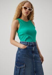 Green ribbed tank top paired with a blue denim skirt featuring side pockets and a button closure, displayed against a neutral background.