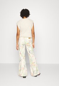 Top sin mangas beige de punto combinado con pantalones acampanados con estampado floral en colores pastel, con una tela suave y texturizada y costuras laterales.