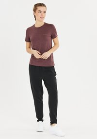 Bordeauxfarbenes T-Shirt mit kurzen Ärmeln und Rundhalsausschnitt, kombiniert mit schwarzen Jogginghosen. Das Outfit bietet eine lockere Passform und einen weichen Stoff.