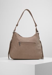 Borsa in pelle taupe con spalline regolabili e una piccola tasca frontale con zip, esposta su un piedistallo bianco su uno sfondo grigio.