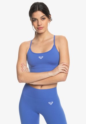 Blue ribbed sports bra with thin straps and a small heart logo, paired with matching blue leggings featuring a similar logo on the waistband.