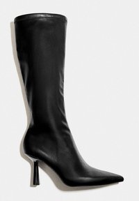 Fekete térd fölé érő bőr csizma hegyes orral és karcsú magas sarokkal, oldalnézetből, fehér háttéren.