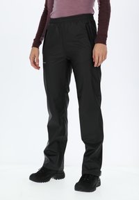Pantaloni neri impermeabili con cintura elastica, tasche laterali e una texture liscia, abbinati a scarpe nere resistenti.