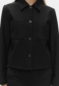 Sort skræddersyet jakke med krave, to forlommer og skjult knaplukning. Glat stof med en struktureret form.