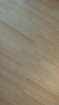 Superficie de madera clara con una textura suave, que presenta variaciones naturales en el veteado y tonos de color en beige pálido y marrón claro.