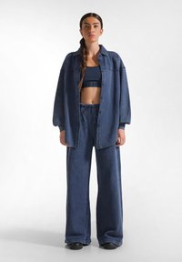 Mörkblå oversized denimskjorta med knappar, matchande vida byxor och en figurnära mörkblå crop top. Slät textur, avslappnad design.