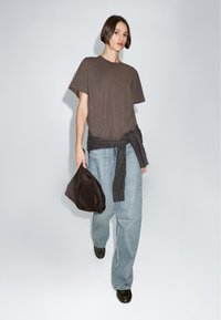 T-shirt marrone a maniche corte, jeans a gamba larga blu chiaro, borsa marrone scuro e scarpe nere. Il t-shirt è annodato in vita.