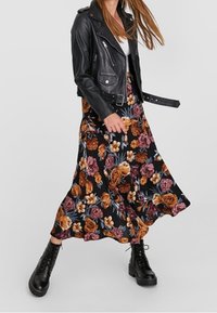 Zwarte maxi-jurk met florale print in oranje en roze rozen, gecombineerd met een zwart leren motorjack en zwarte laarzen met veters.