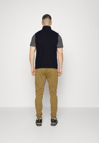 Marineblaue Fleece-Weste, graues, kurzärmliges Hemd, beige Hose und schwarze Sneakers. Einfaches Design mit Kragen und lässiger Passform, keine sichtbaren Muster.