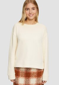 Crème-kleurige sweatshirt met een ronde halslijn en verlaagde schouders, met een gestructureerde stof. Gecombineerd met een geruite rok in oranje en wit.