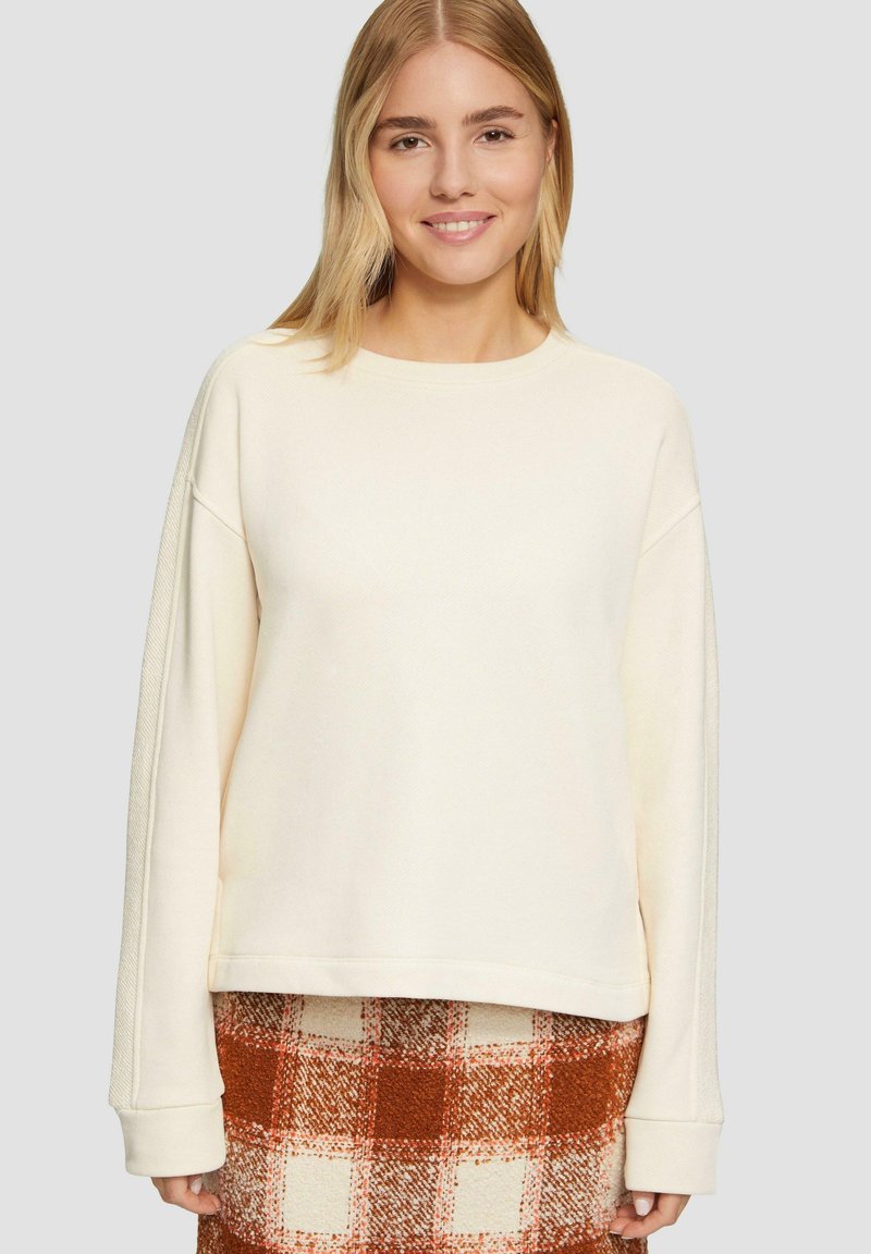 Crème-kleurige sweatshirt met een ronde halslijn en verlaagde schouders, met een gestructureerde stof. Gecombineerd met een geruite rok in oranje en wit.