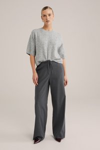 Pelēkas adītas īsām piedurknēm blūze, kas saskaņota ar tumši pelēkiem plašiem biksēm ar aukliņu viduklī, ar smalku svītraina rakstu.