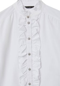 White blouse featuring a ruffled front detail, round metallic buttons, and a high collar design. Smooth fabric with a crisp appearance.