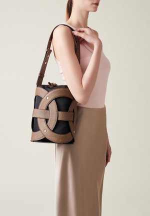 Braune, strukturierte Ledertasche mit schwarzem Boden, die ein markantes geflochtenes Design und einen verstellbaren Trageriemen aufweist, der über der Schulter getragen wird.