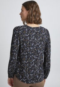 Blusa floreale navy con maniche lunghe, caratterizzata da un design con spalle a palloncino e piccoli motivi floreali bianchi e dorati su uno sfondo scuro.