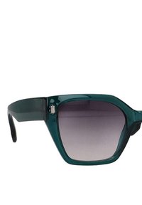 Gafas de sol de plástico verde con montura angular, lentes gradientes en tonos grises y un acento de logo plateado en la patilla izquierda.