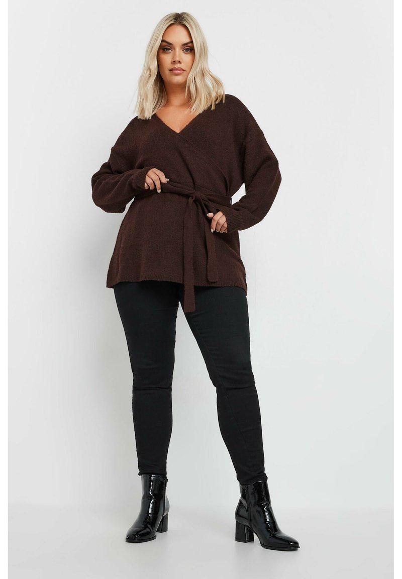 Brun stickad omslagskofta med ett knytbälte, långa ärmar och V-ringning. Kombinerad med svarta slim-fit jeans och glansiga klackade ankelstövlar.