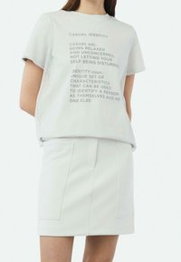 T-shirt en coton gris clair à manches courtes avec des définitions imprimées, assorti d'une jupe gris clair avec deux poches frontales.