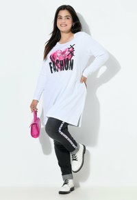 Witte lange mouwen tuniek met "FASHION" graphic en roze hart. Donkergrijze spijkerbroek met witte zijkanten. Zwarte veterschoenen. Roze handtas.