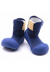 Botines de tela azul con una suela de goma texturizada. Presenta acentos de rayas amarillas y blancas en el puño. Diseñados con una parte superior de estructura flexible.