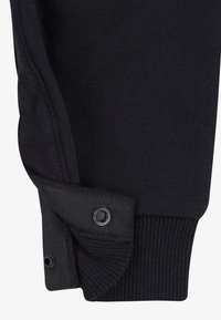 Svarta bomullsjoggers med ribbad mudd och knäppdetalj vid ankeln. Slät textur med rena sömmar och minimal design.