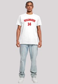 Balts kokvilnas T-krekls ar uzrakstu "WILDCATS" un numuru "14" sarkanā krāsā. Saskaņots ar gaiši ziliem džinsiem un baltām sporta apaviem. Gluda tekstūra.