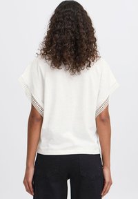 Cream cotton top with short, wide sleeves featuring lace accents at the edges. The back is simple and slightly loose-fitting.