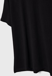 Czarna koszulka, casualowy design z krótkimi rękawami, wykonana z miękkiego bawełnianego materiału. Dół jest lekko zaokrąglony, z gładką teksturą.