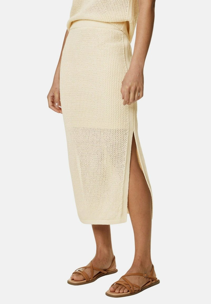 Strikket cremefarvet midi-nederdel med sidesplitter, tekstureret stof og en tætsiddende talje. Kombineret med brune sandaler med stropper.