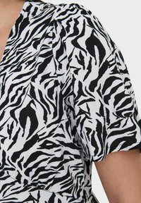 Tissu à motifs zébrés noir et blanc avec des manches courtes et un décolleté en V ; présente une texture lisse et un léger plissement à l'épaule.