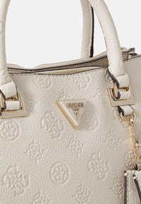 Bolso de piel blanca texturizada con herrajes dorados, que cuenta con una placa de logo triangular y patrones en relieve en la superficie.